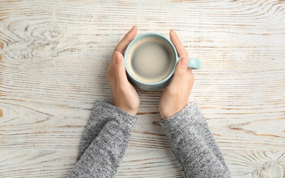 Photo of Young woman with cup of delicious hot coffee on wooden background, top view