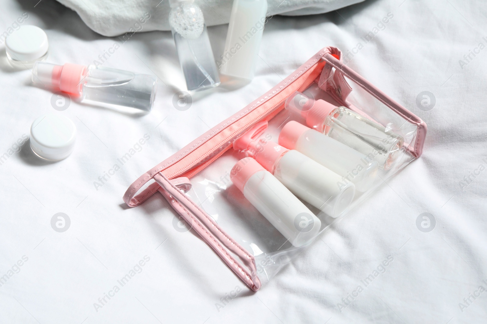 Photo of Cosmetic travel kit. Plastic bag with small containers of personal care products on bed