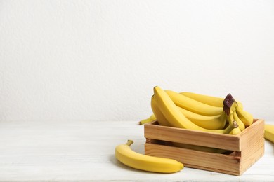 Photo of Ripe yellow bananas and crate on white wooden table. Space for text