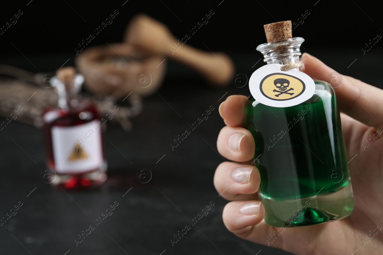 Photo of Woman holding glass bottle of poison with warning sign over table, closeup. Space for text