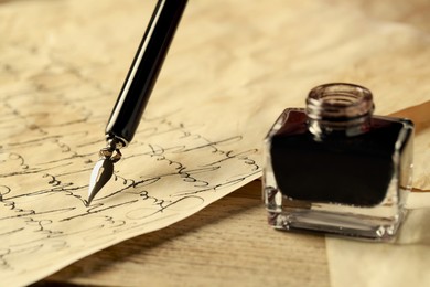 Photo of Writing with fountain pen on vintage parchment near inkwell at wooden table, closeup