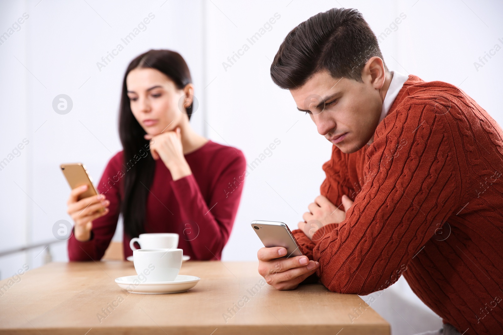 Photo of Couple addicted to smartphones ignoring each other in cafe. Relationship problems