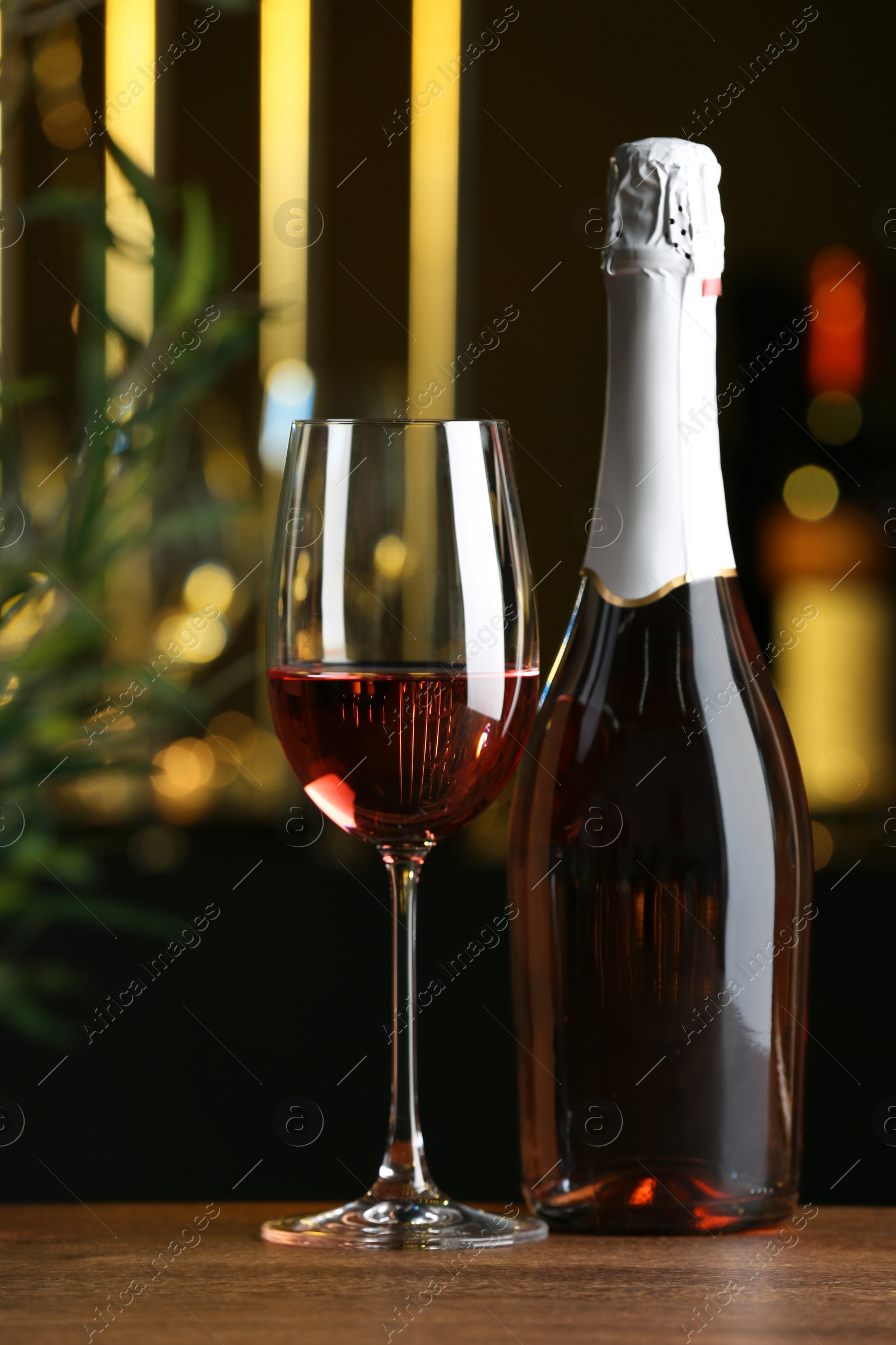 Photo of Bottle and glass of delicious rose wine on wooden table in bar