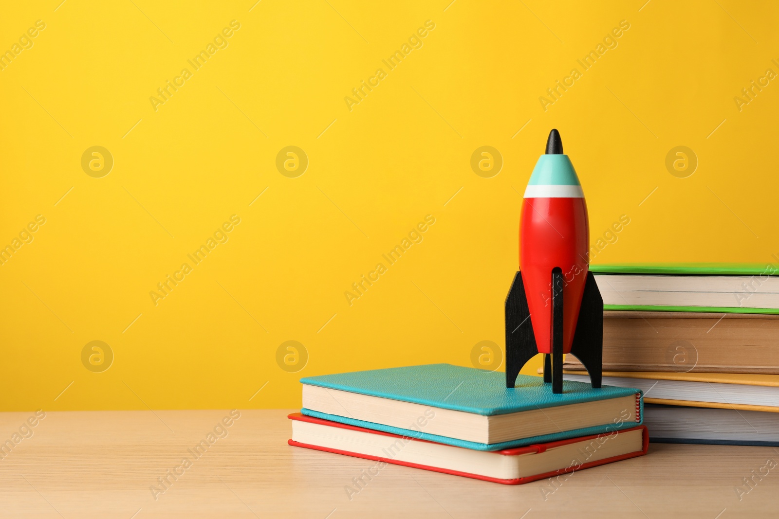 Photo of Bright toy rocket and school supplies on wooden table. Space for text