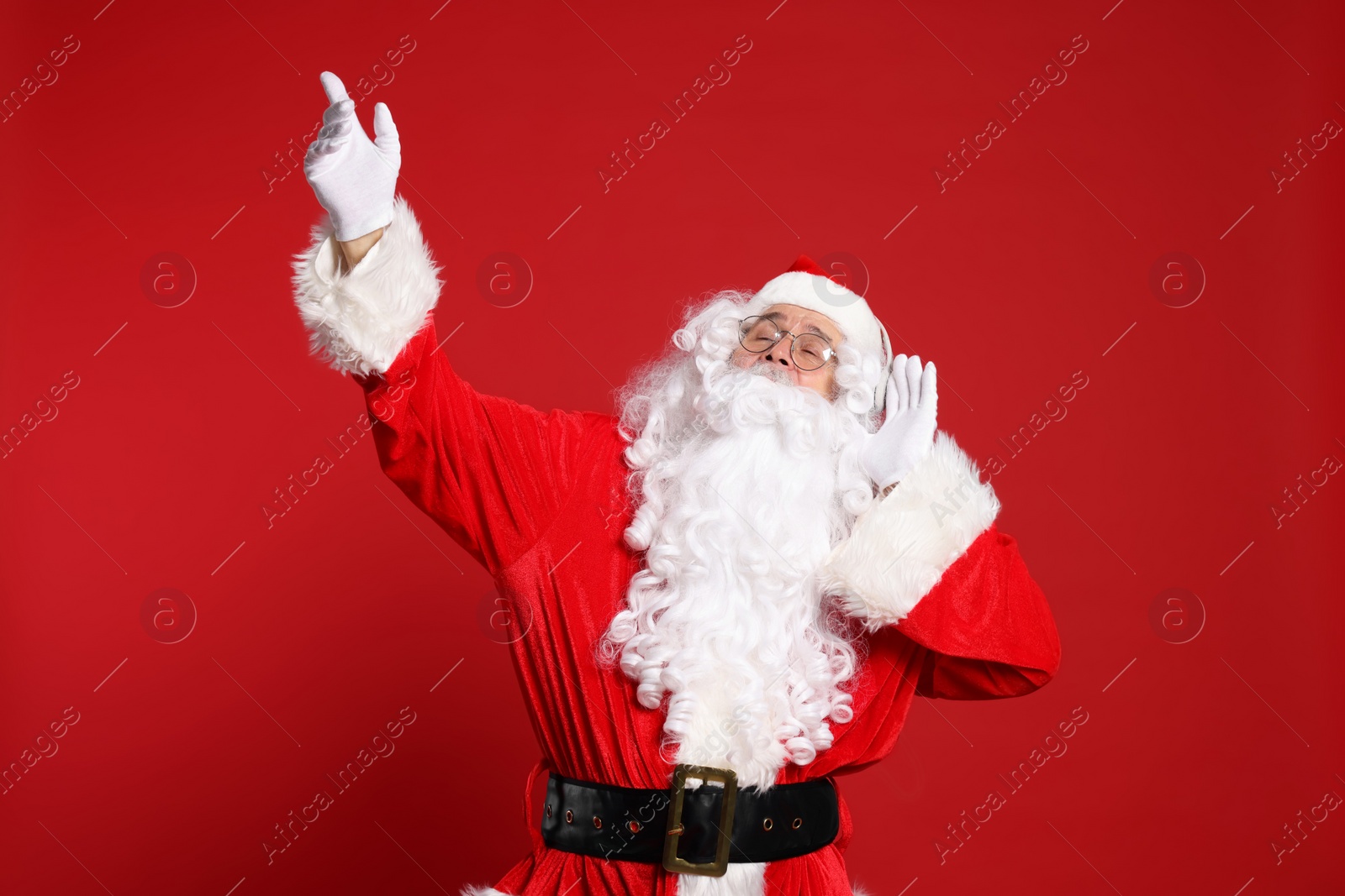 Photo of Merry Christmas. Santa Claus in headphones listening to music on red background