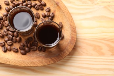 Photo of Shot glasses with coffee liqueur and beans on wooden table, top view. Space for text