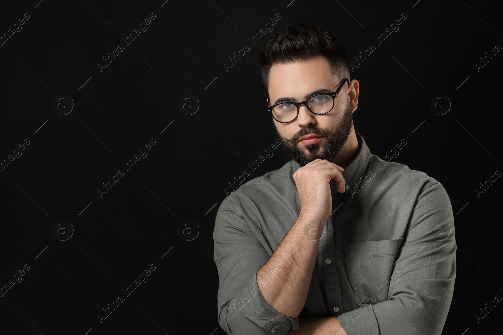 Photo of Young man with mustache touching face on black background. Space for text