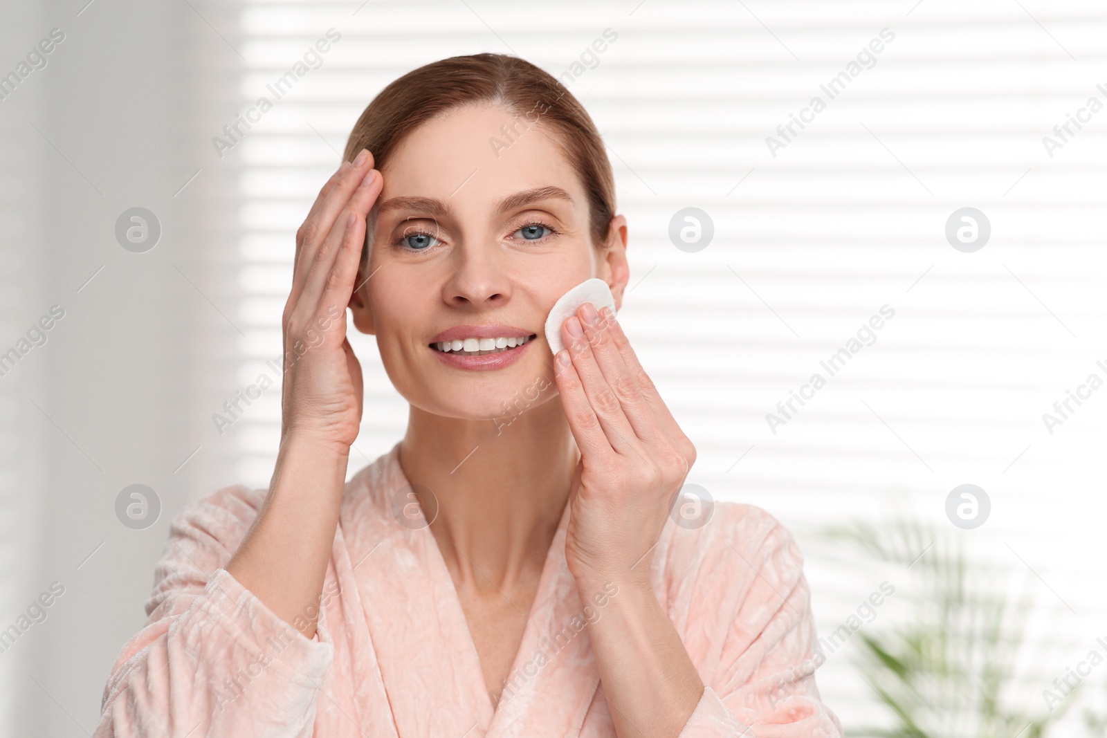 Photo of Beautiful woman removing makeup with cotton pad indoors