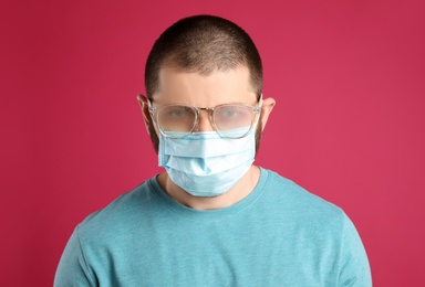 Photo of Man with foggy glasses caused by wearing disposable mask on pink background. Protective measure during coronavirus pandemic