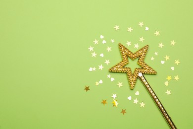 Photo of Beautiful golden magic wand and confetti on light green background, flat lay. Space for text