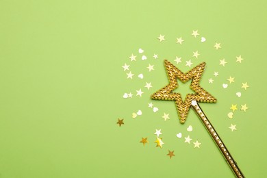 Beautiful golden magic wand and confetti on light green background, flat lay. Space for text