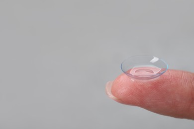 Photo of Woman holding contact lens on grey background, closeup. Space for text