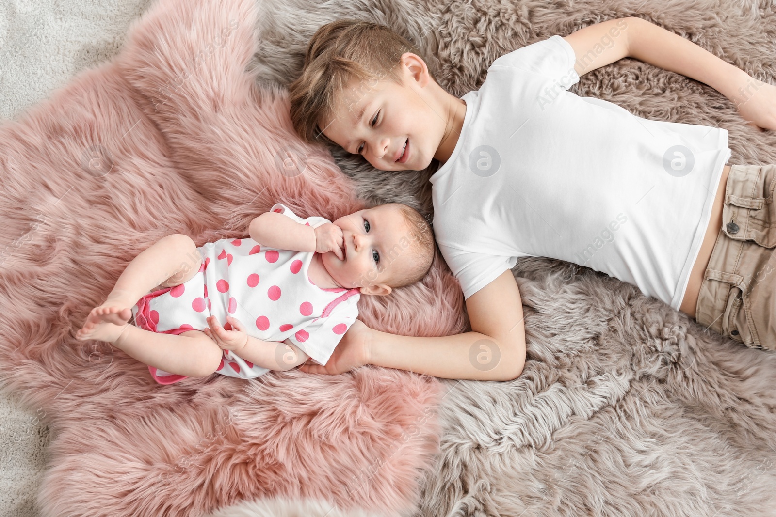 Photo of Cute little baby with elder brother lying on soft fluffy plaid at home