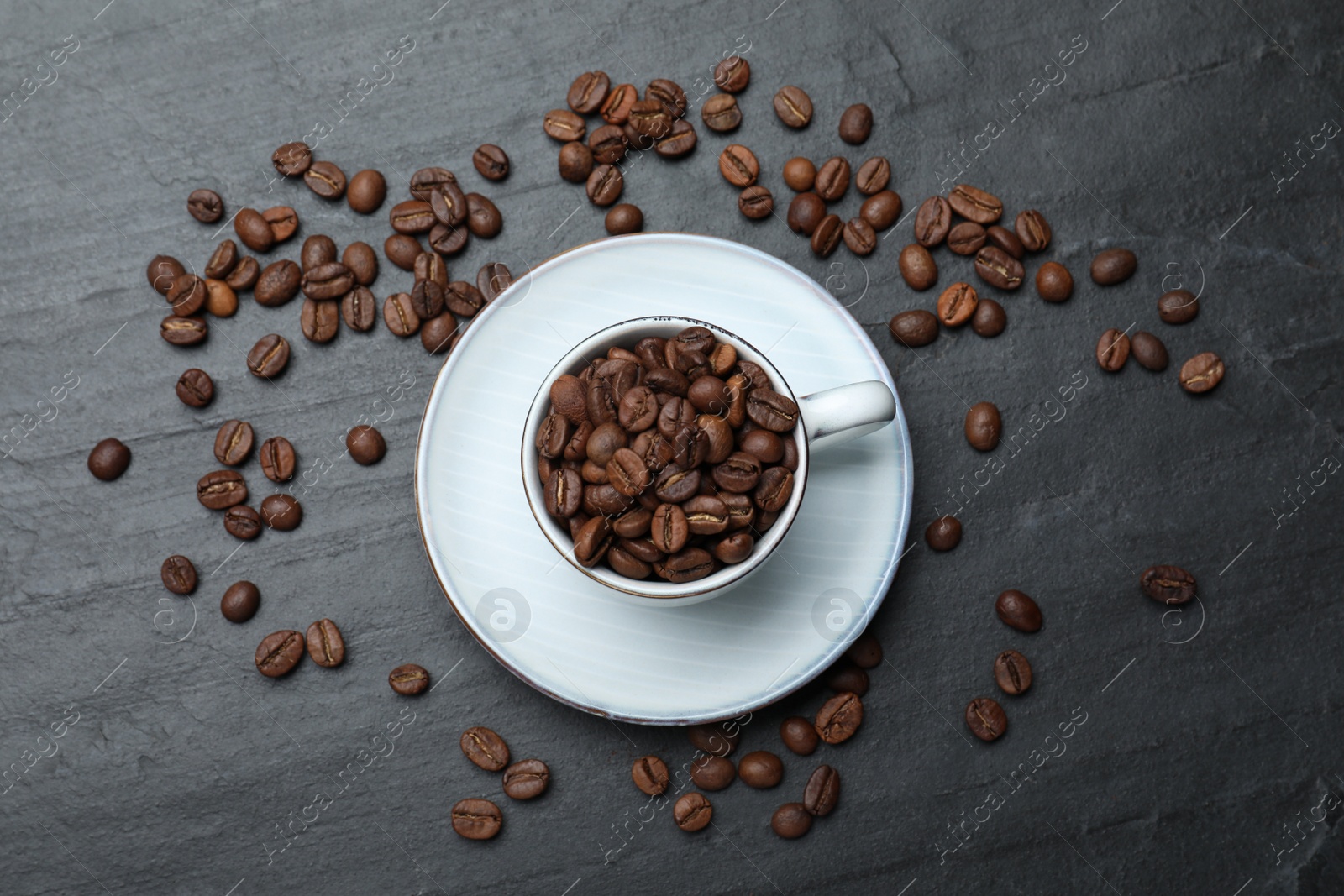 Photo of Cup with roasted coffee beans on black table, flat lay