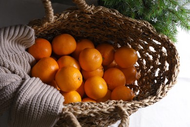 Photo of Net bag with fresh ripe tangerines and fir tree branch on white cloth, above view