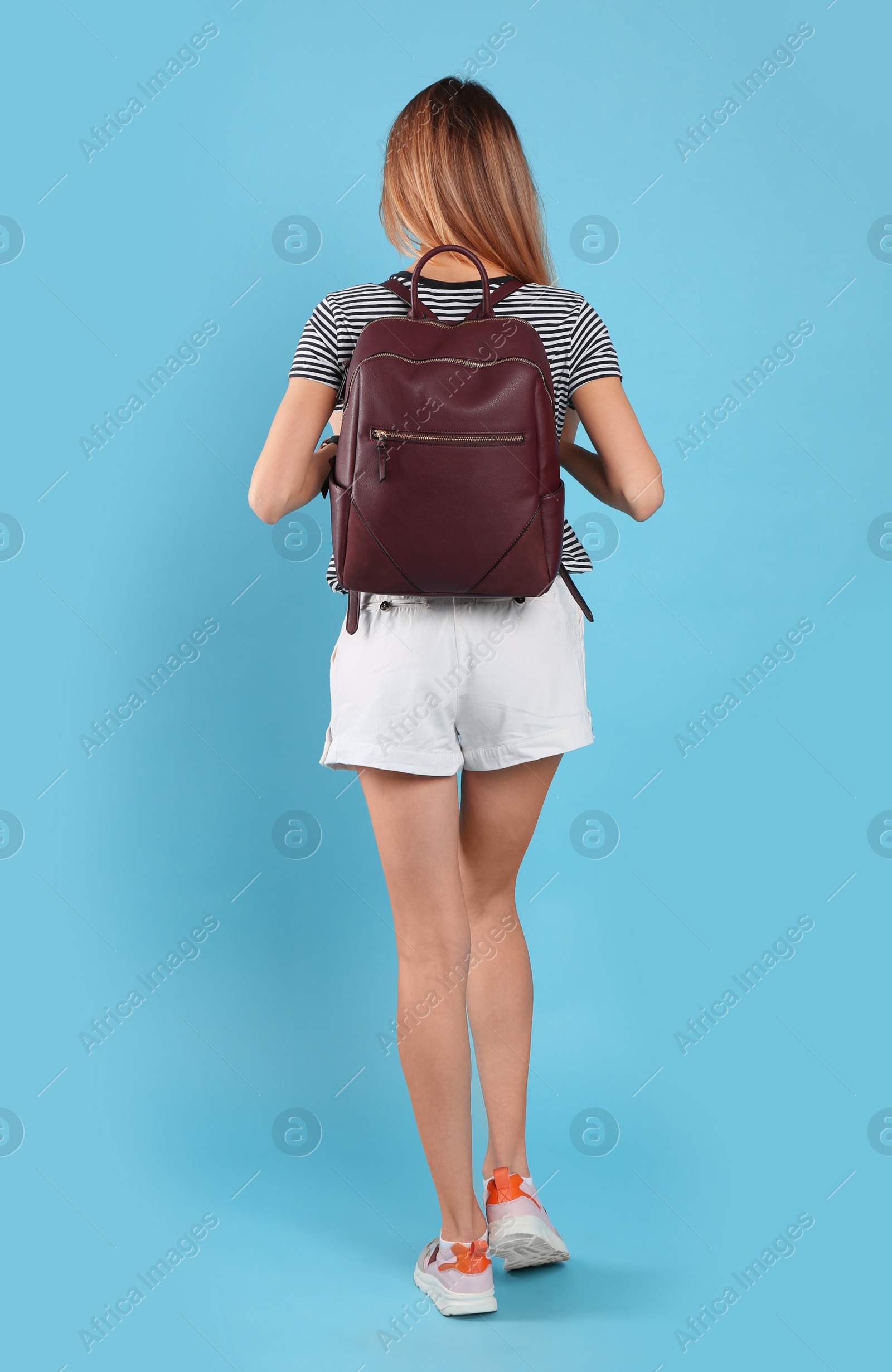 Photo of Woman with backpack on light blue background, back view