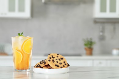 Photo of Tasty refreshing drink with orange and cookies on white marble table in kitchen. Space for text