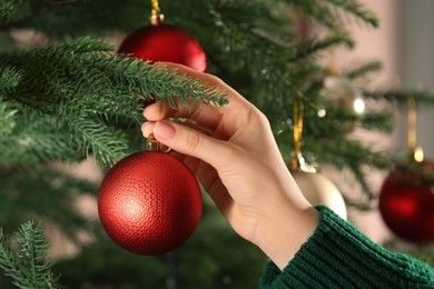 Photo of Woman decorating Christmas tree with beautiful red bauble, closeup