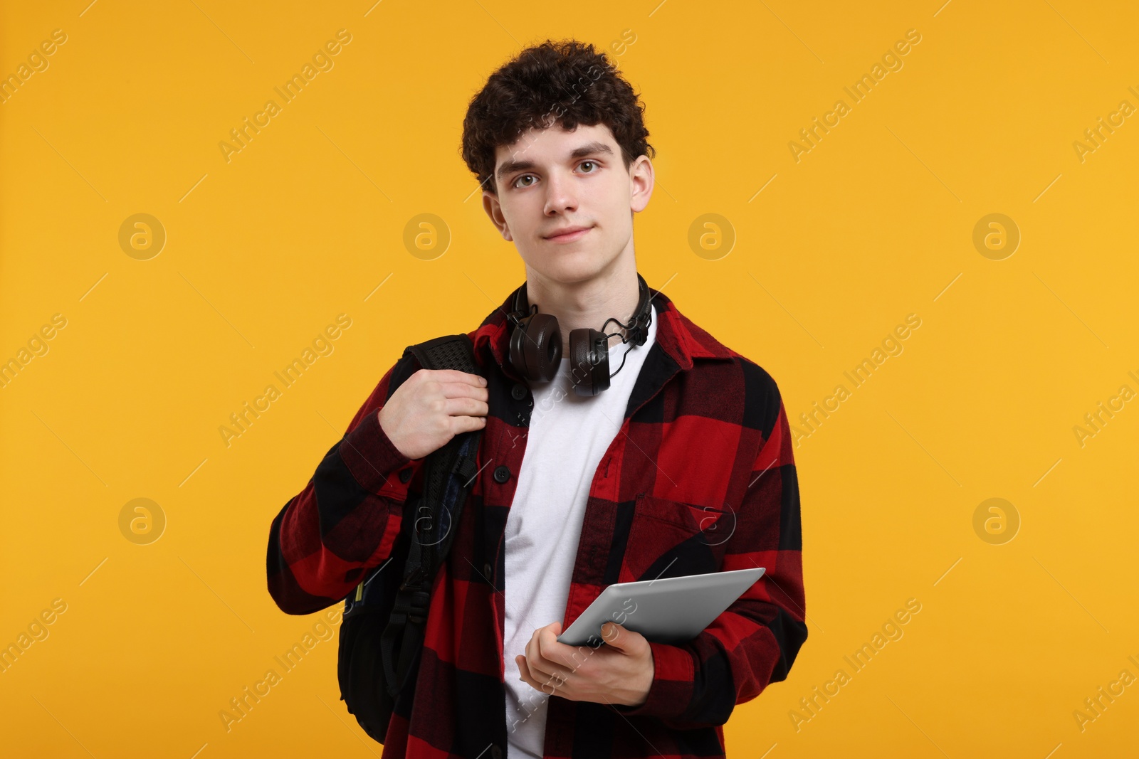 Photo of Portrait of student with backpack, headphones and tablet on orange background