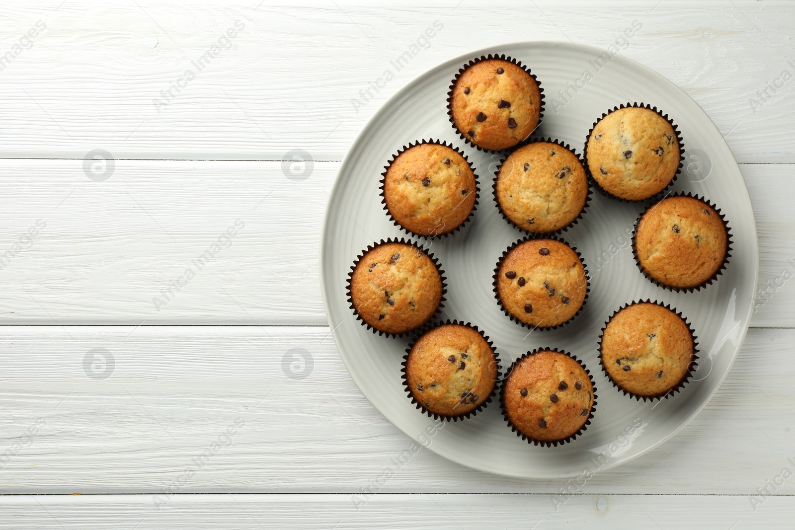 Photo of Delicious freshly baked muffins with chocolate chips on white wooden table, top view. Space for text