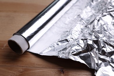 Roll of aluminum foil on wooden table, closeup