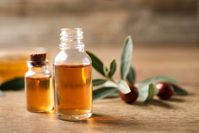 Glass bottles with jojoba oil on wooden table. Space for text