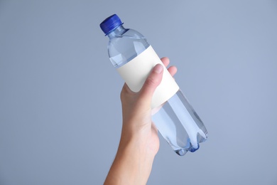 Photo of Woman holding plastic bottle with soda water on light  grey background, closeup