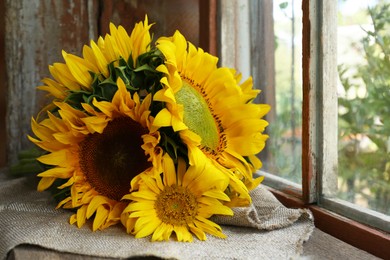 Photo of Beautiful sunflowers on cloth near window indoors