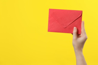 Photo of Woman holding red paper envelope on yellow background, closeup. Space for text