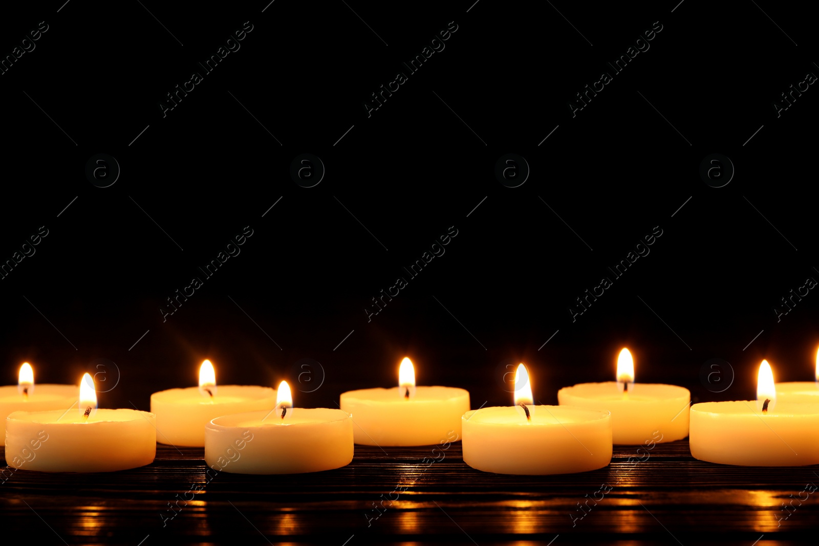 Photo of Burning candles on table against black background, space for text