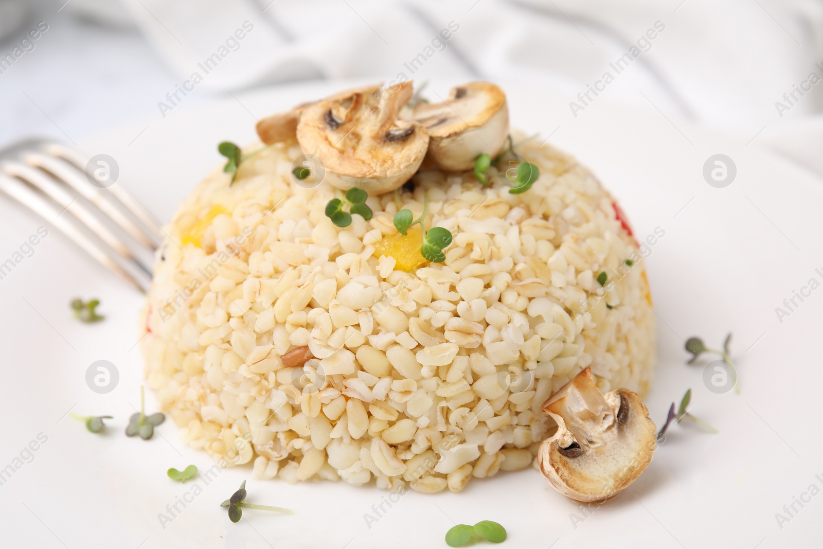 Photo of Delicious bulgur with vegetables, mushrooms and microgreens on table, closeup