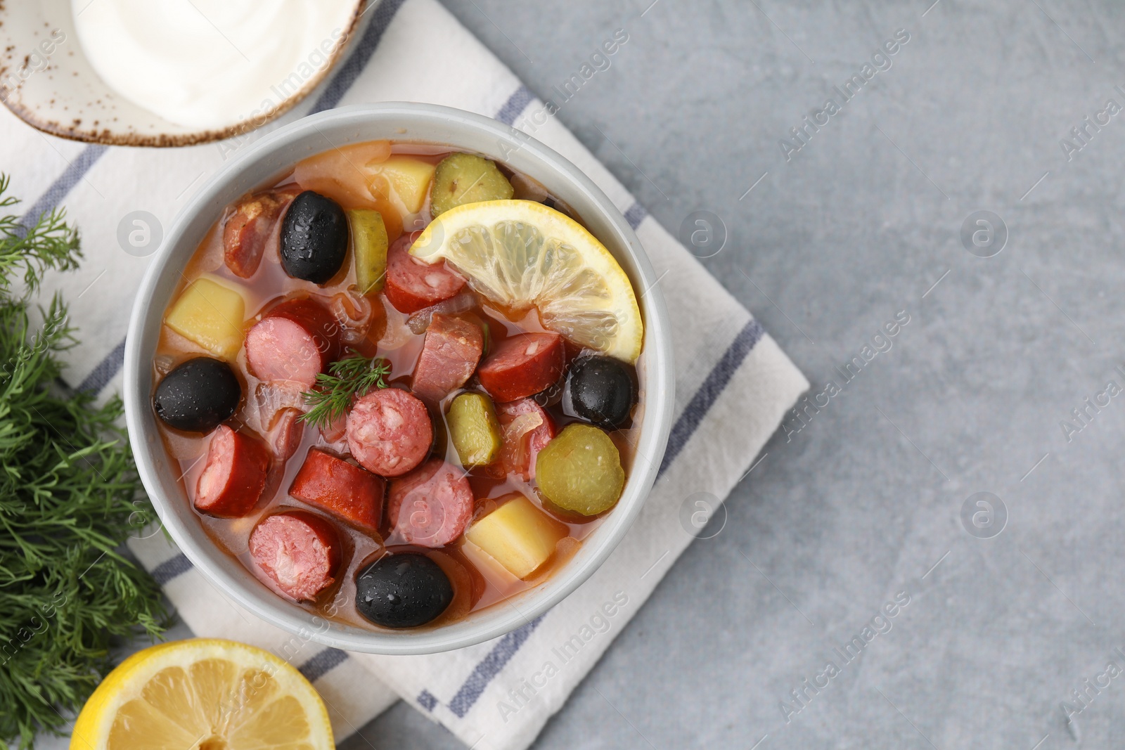 Photo of Meat solyanka soup with thin dry smoked sausages served on grey table, flat lay. Space for text