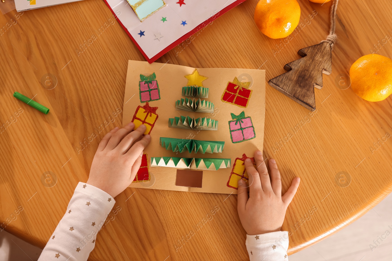 Photo of Little child with beautiful Christmas card at table, top view