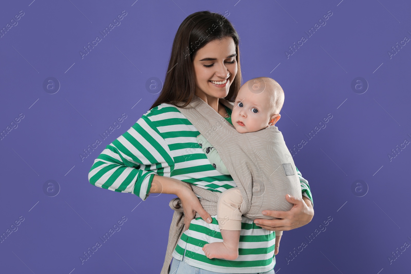 Photo of Mother holding her child in sling (baby carrier) on purple background