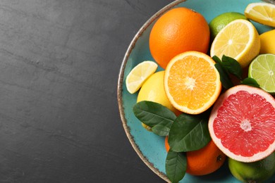 Different cut and whole citrus fruits on black table, top view. Space for text