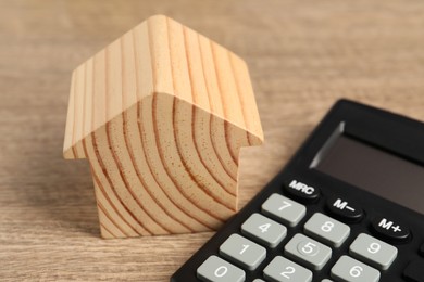 Photo of Mortgage concept. Model house and calculator on wooden table, closeup
