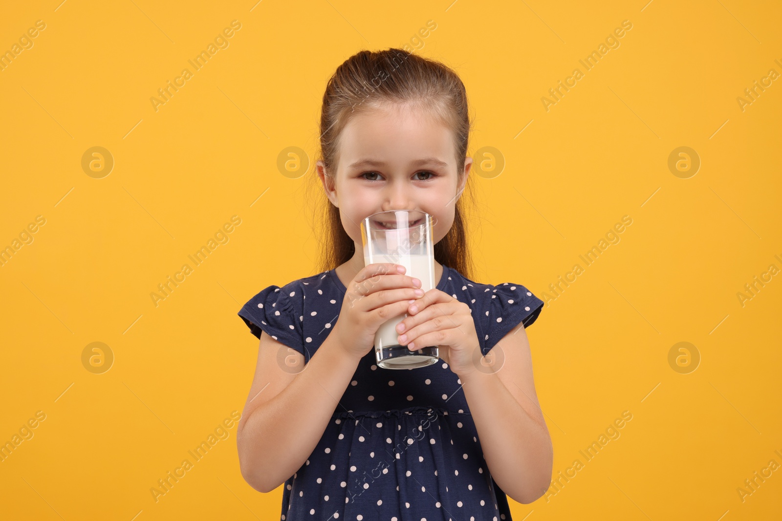 Photo of Cute girl with glass of fresh milk on orange background