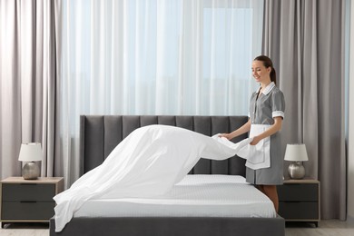 Young maid making bed in hotel room. Space for text