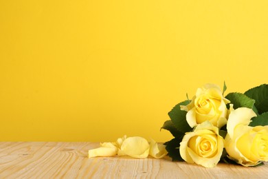 Beautiful fresh roses on wooden table against yellow background. Space for text