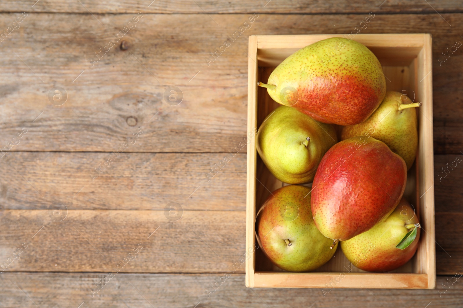 Photo of Crate with ripe juicy pears on brown wooden table, flat lay. Space for text