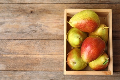 Crate with ripe juicy pears on brown wooden table, flat lay. Space for text