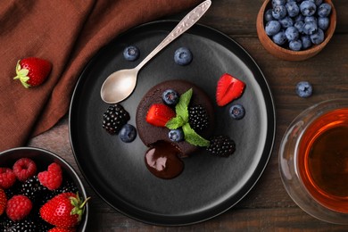 Photo of Plate with delicious chocolate fondant, berries and mint on wooden table, flat lay