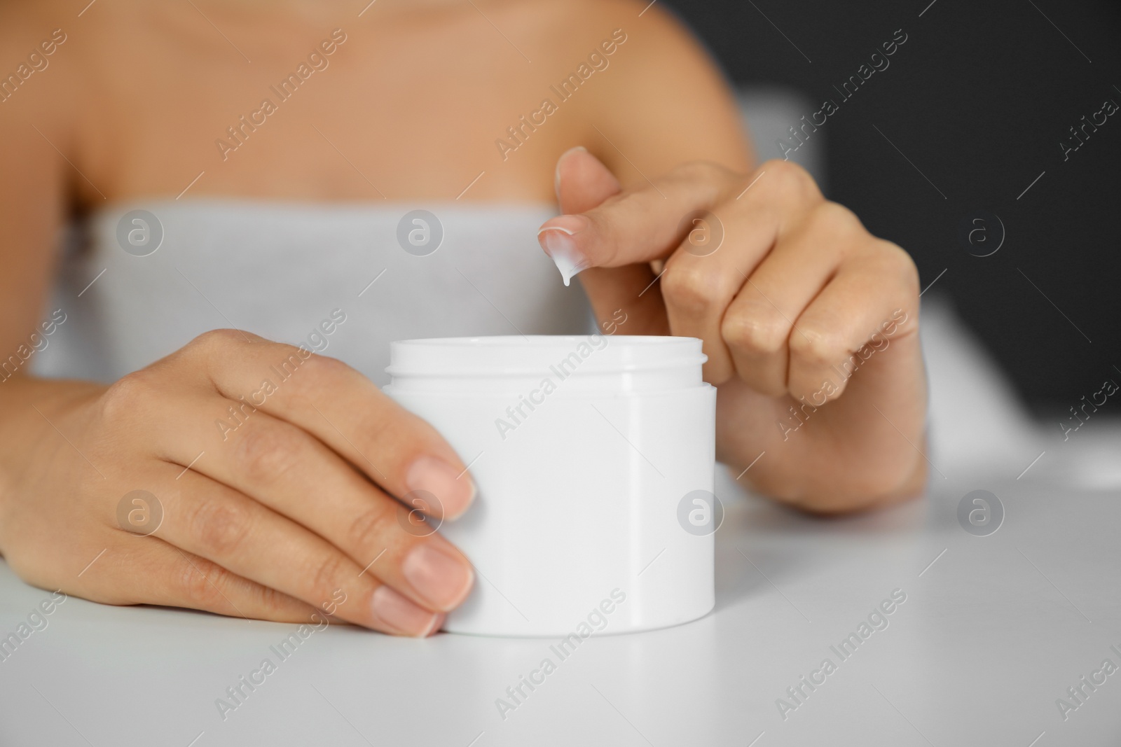 Photo of Woman with jar of moisturizing cream at white table, closeup