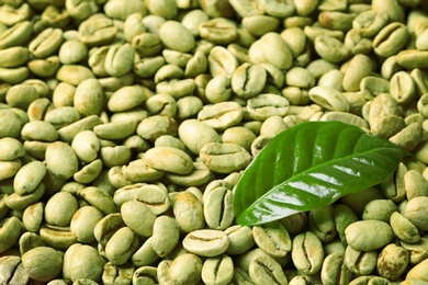 Photo of Green coffee beans and fresh leaf as background, closeup