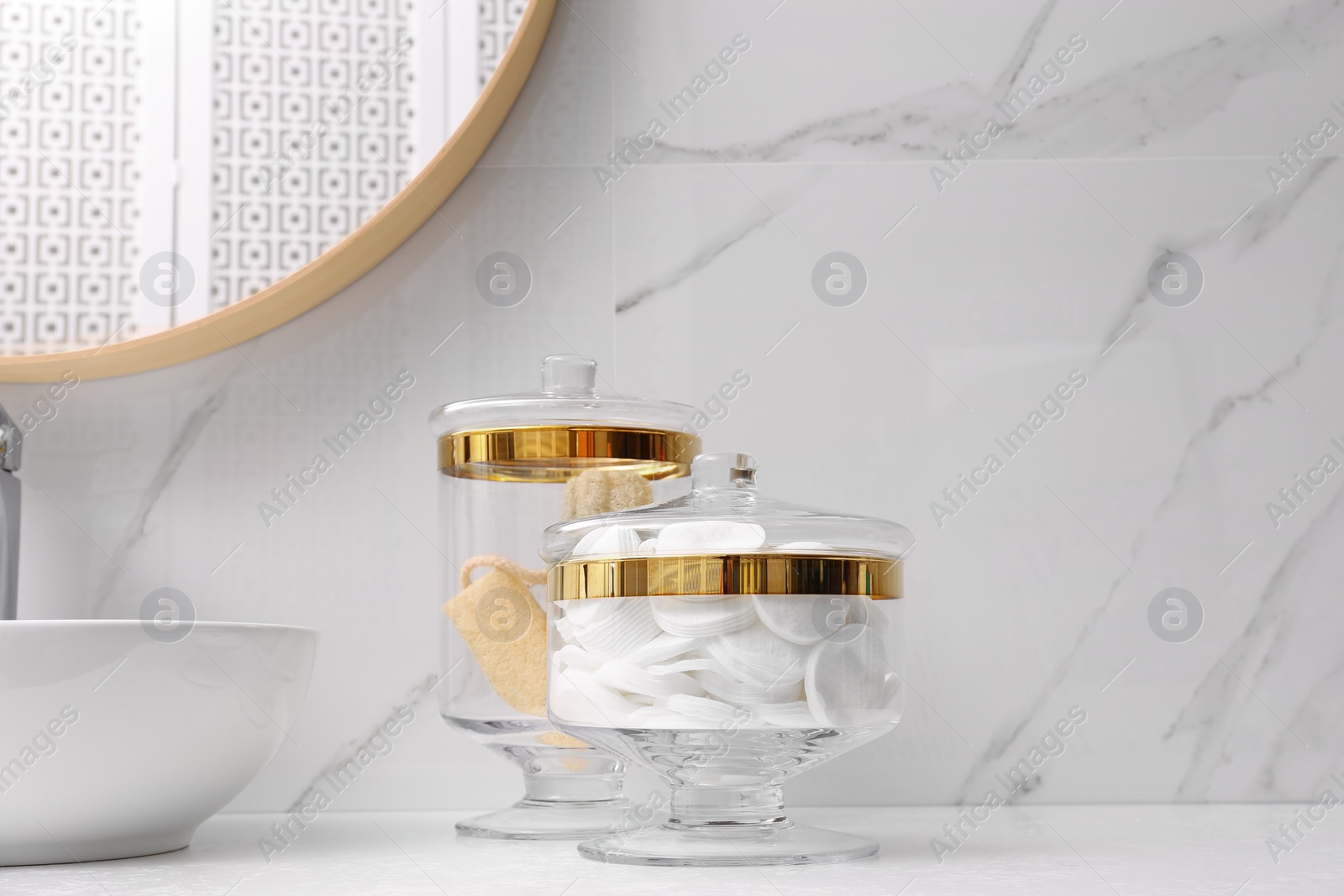 Photo of Glass jars with cotton pads and loofahs on table in bathroom