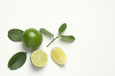 Whole and cut fresh ripe limes with green leaves on white background, flat lay