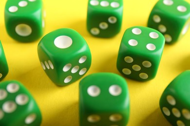 Photo of Many green game dices on yellow background, closeup