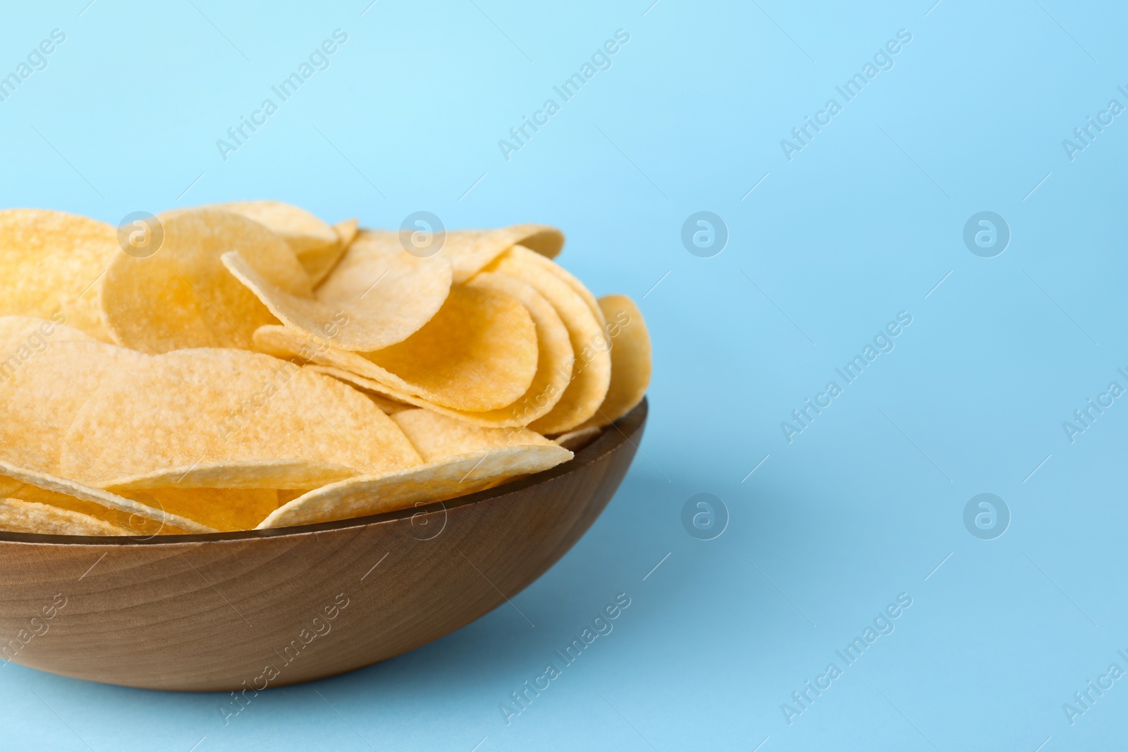 Photo of Bowl with delicious potato chips on light blue background, closeup. Space for text