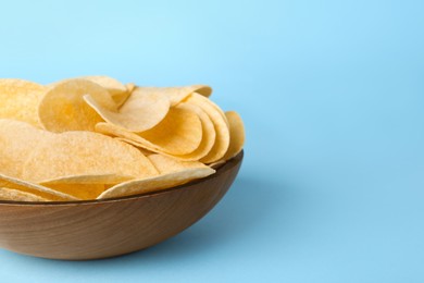 Bowl with delicious potato chips on light blue background, closeup. Space for text