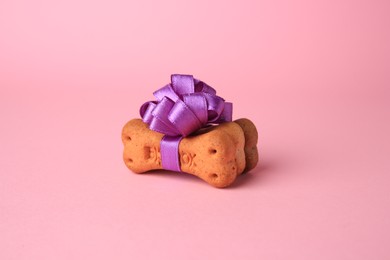 Photo of Bone shaped dog cookies with purple bow on pink background